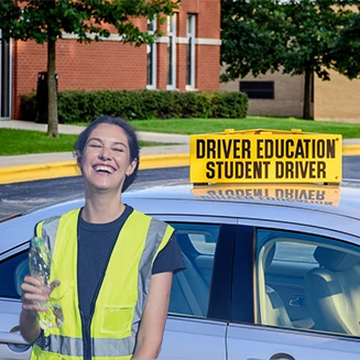 Young woman instructor next to vehicle with driver training sign.