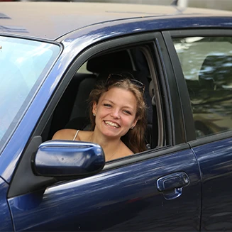 Young woman smiling leaning out of car window.